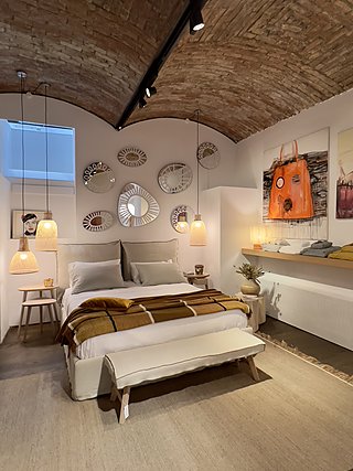 Ausgestelltes Schlafzimmer im Schauraum mit Backsteingewölbe und Hängelampen aus Rattan.