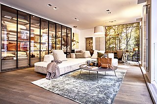 Wohnbereich im Schauraum mit Sofa, Glasvitrine und Essplatz im Hintergrund.