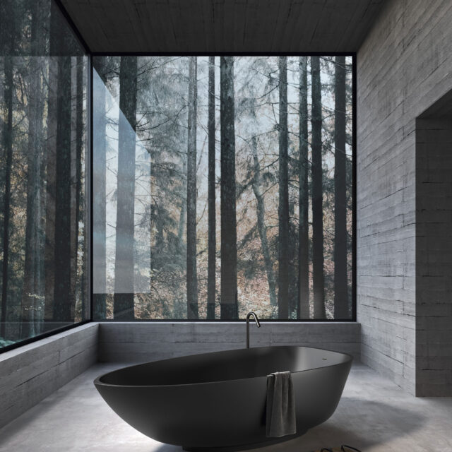 Modernes Badezimmer mit freistehender schwarzer Badewanne von Rexa Design vor einer großen Glaswand mit Blick auf einen Wald. Minimalistisches Design mit Betonwänden und einer ruhigen Atmosphäre, ideal für Entspannung und Wohlbefinden.