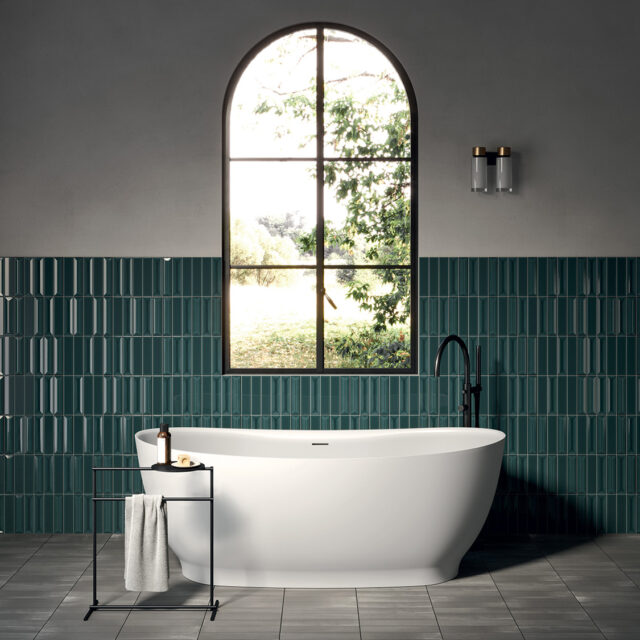 Modernes Badezimmer mit freistehender weißer Badewanne von Rexa Design, vor einer stilvollen, türkisfarbenen Wandverkleidung und einem großen, gewölbten Fenster mit Blick ins Grüne. Minimalistisches, elegantes Design mit natürlicher Lichtquelle, das zur Entspannung und Erholung einlädt.